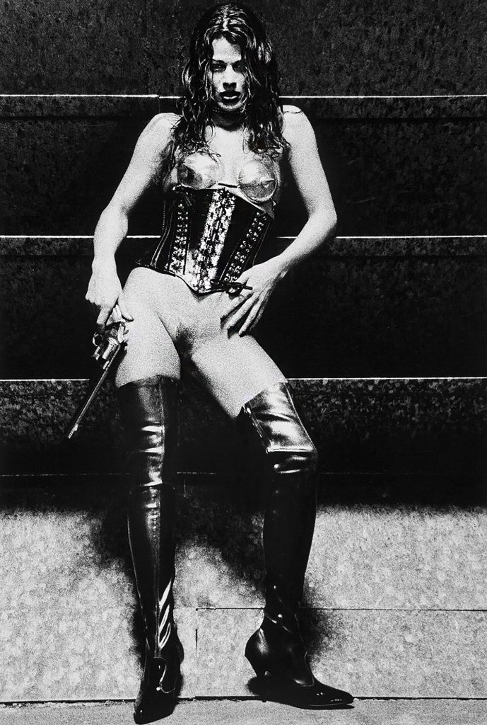 A young woman wearing a fetish outfit corset with spikes high boots and long barrel pistol